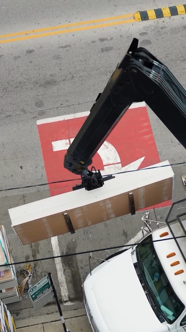 Boom crane lifting drywall bundle from delivery truck
